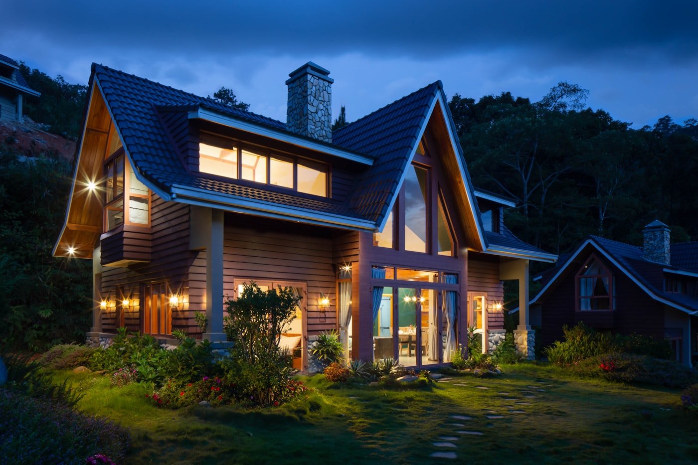 Wood and stone home with a steep shingle roof at dusk